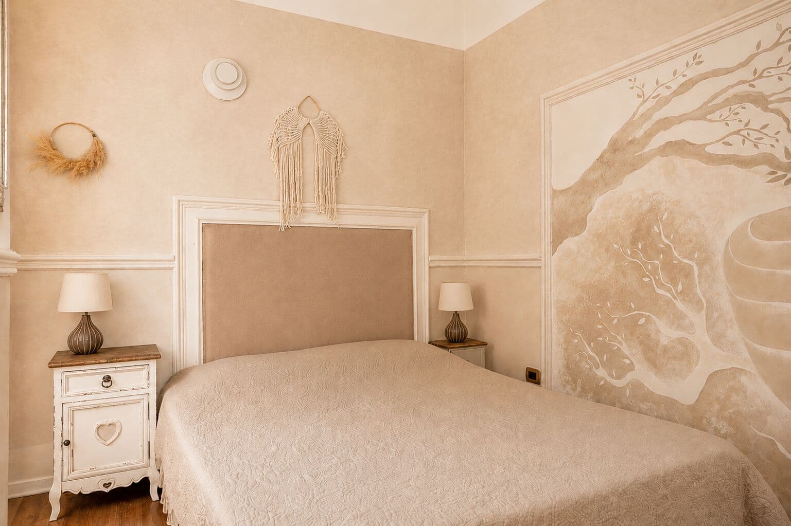 Cocoon room with upholstered headboard, hand-painted olive tree mural and macramé wall hanging